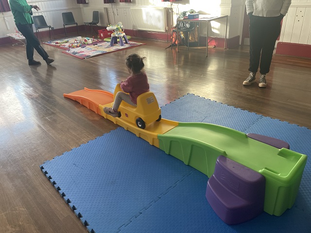 Young girl riding a plastic car on a plastic ramp