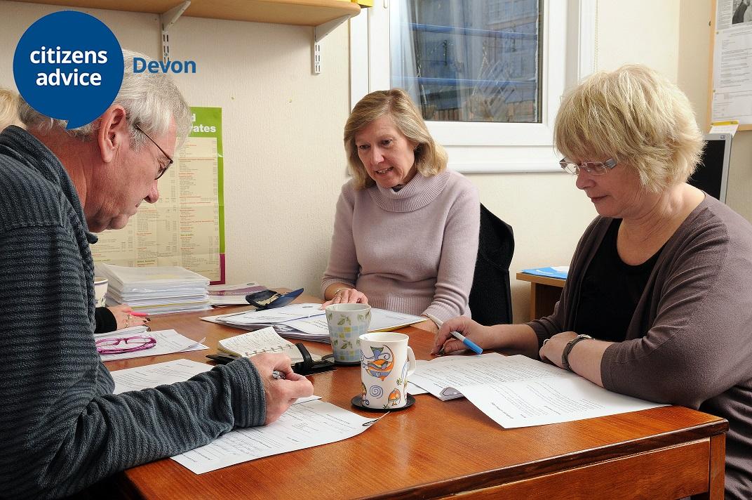 Two older people sat with a lady looking at documents over a table with cups of tea