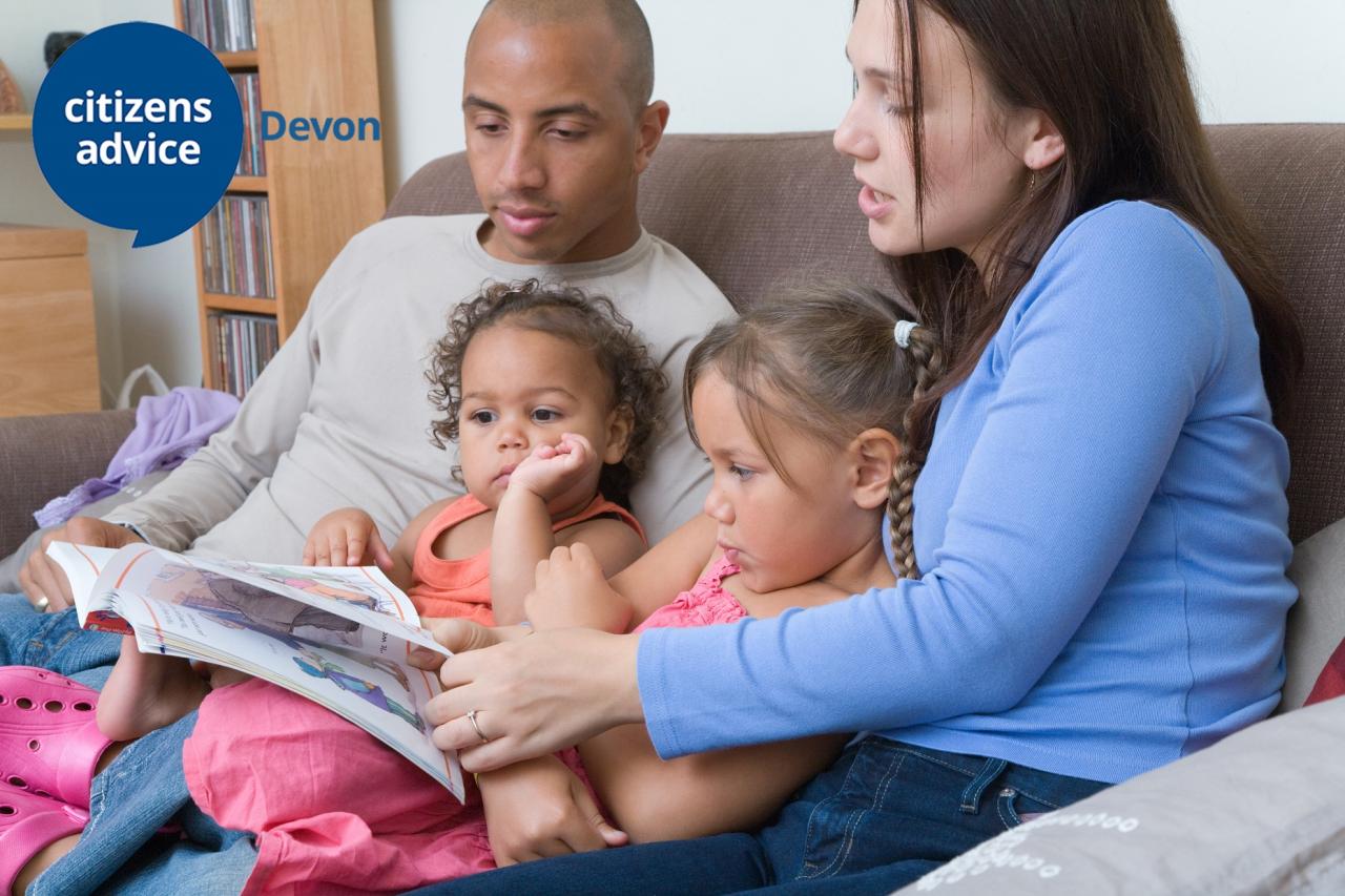 Young black male and white female sitting on a sofa with two young girls reading a book
