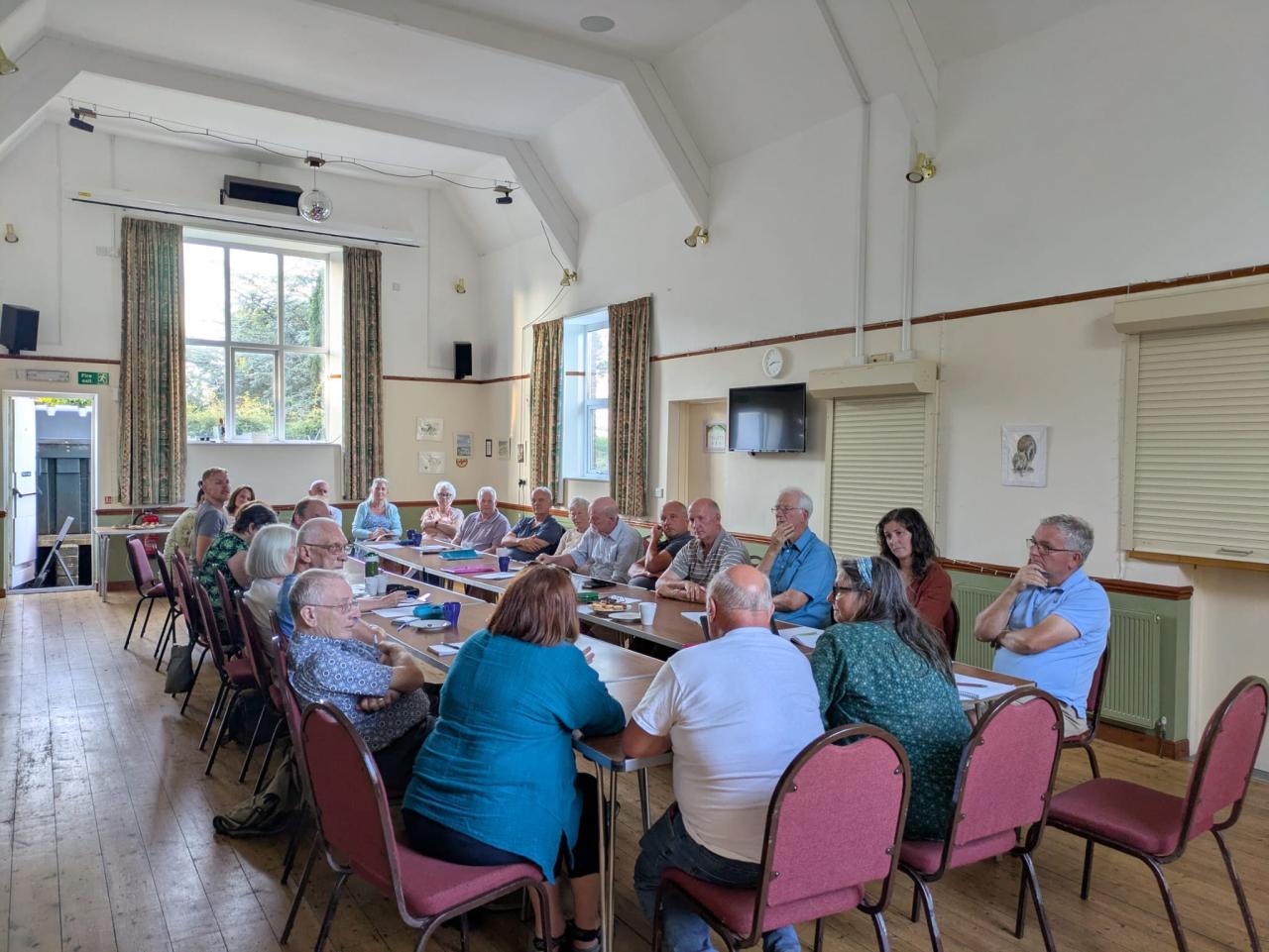 Mid Devon Cluster group meeting, group of people chatting round a table in a Village Hall