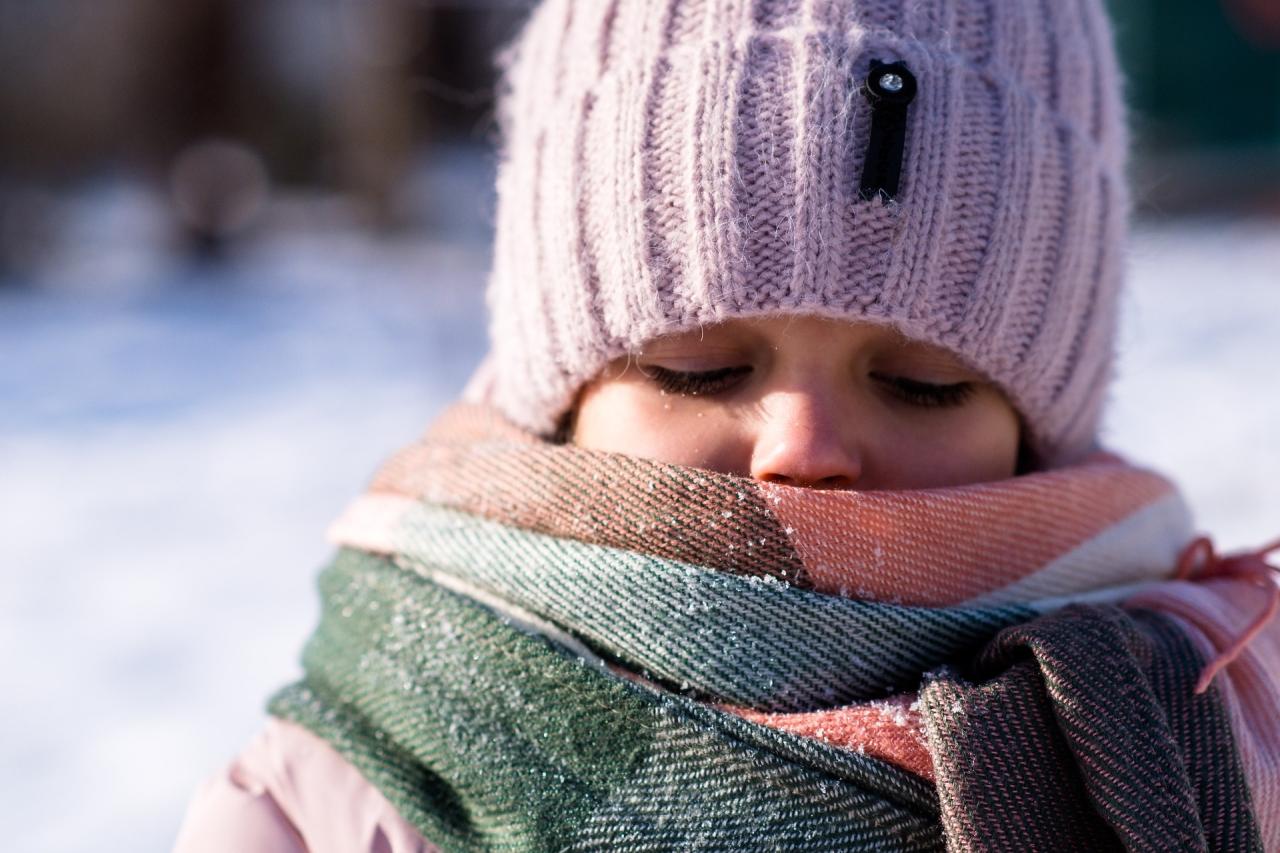 Young girl approximately aged 5 with hat and scarf mostly covering her face. cold snowy background that is blurred. 