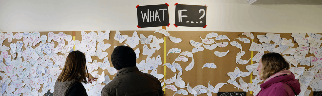 three people looking at a wall of notes with the text what if...