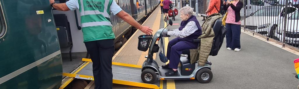 woman on a motorised chair being assisted on to a train