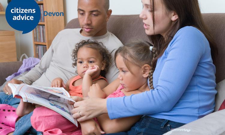 Black adult male and white adult female reading with two small children 