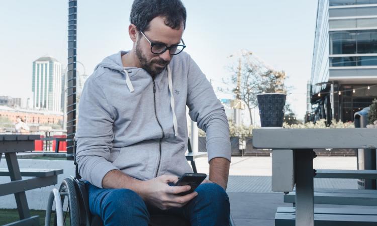 Serious adult male in wheelchair looking down at phone (PIP)