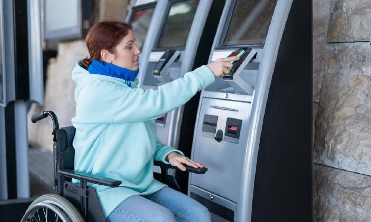 woman in wheelchair purchasing a travel ticket at a machine