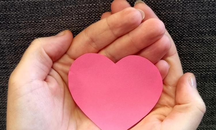 pink paper heart held in a pair of hands