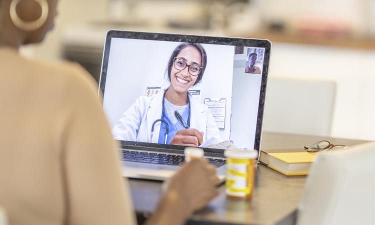 Online medical consultation with a female doctor in a white lab coat showing on a laptop screen. 