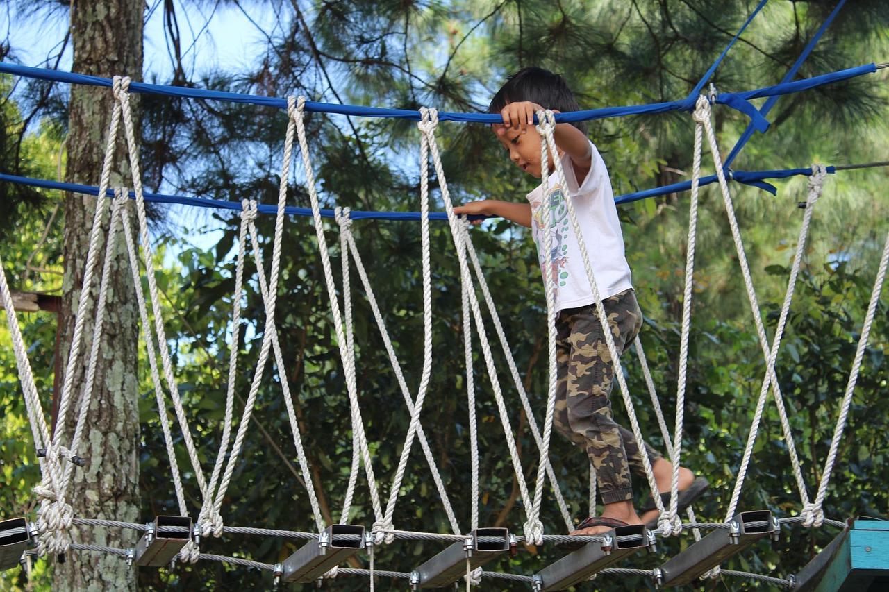 young boy climbing over a rope bridge