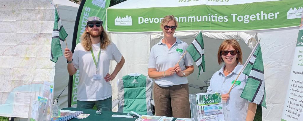 Three DCT staff members at a stand, holding flags on a sunny day